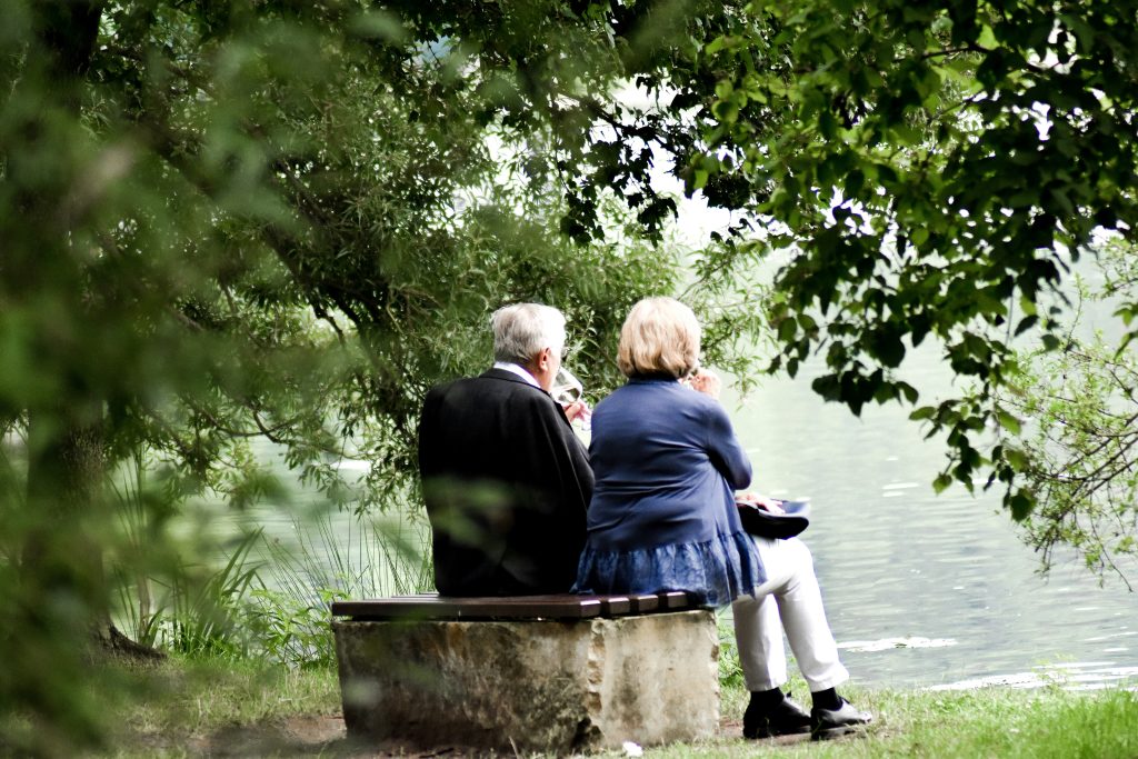 Pareja de personas mayores disfrutando de una conversación al aire libre, junto a un lago, en un entorno tranquilo y natural.