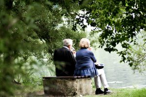 Pareja de personas mayores disfrutando de una conversación al aire libre, junto a un lago, en un entorno tranquilo y natural.