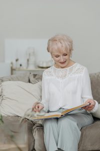 Mujer mayor disfrutando los beneficios audífonos modernos mientras lee un libro en casa.