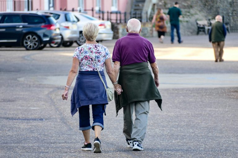 Pareja mayor caminando de la mano, representando bienestar, independencia y equilibrio entre pérdida auditiva y autonomía.