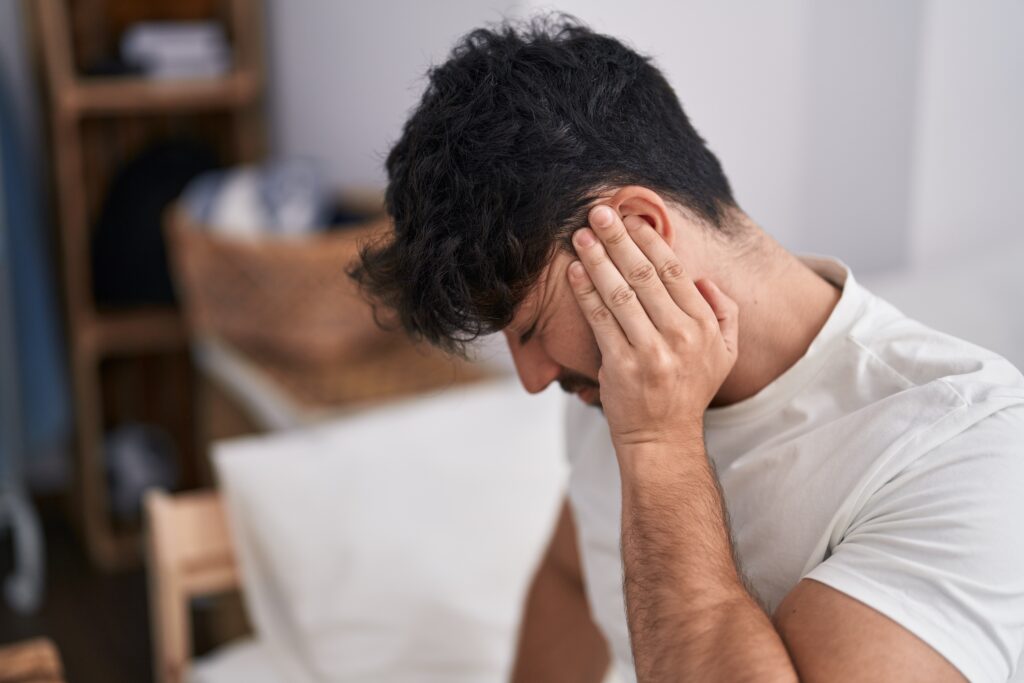 Hombre sentado en la cama con la mano en el oído por tinnitus pulsátil